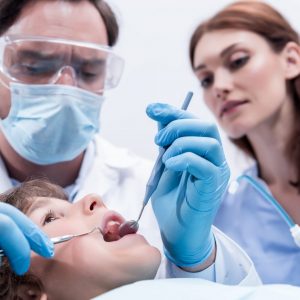 low-angle-view-of-dentists-examining-teeth-of-little-boy-at-dentist-office-e1617040347874